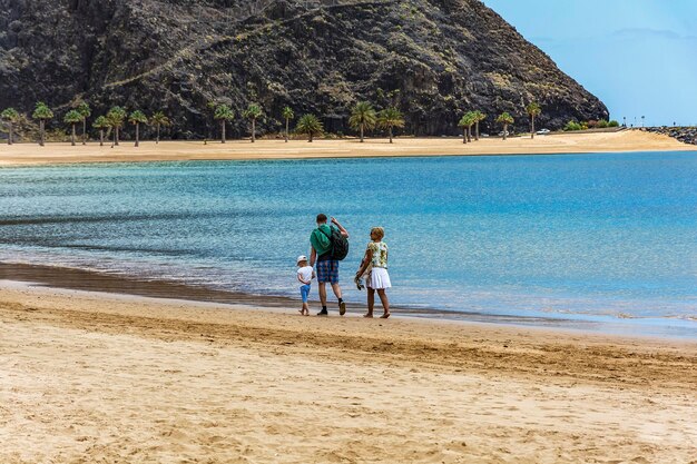 A man with a woman and a child walking along a deserted beach near the water