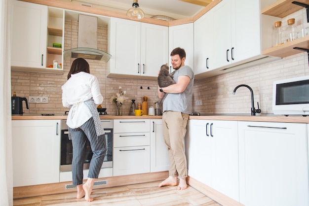 Man with woman at the kitchen cooking holding cat on hands