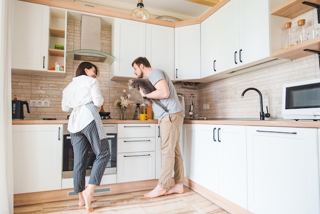 Man with woman at the kitchen cooking holding cat on hands