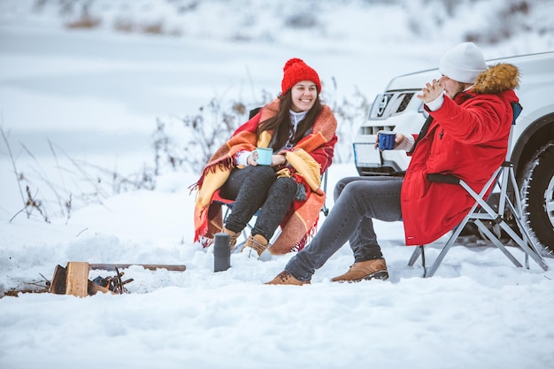 Man with woman sitting on chairs near camp fire in winter time. car travel. active lifestyle