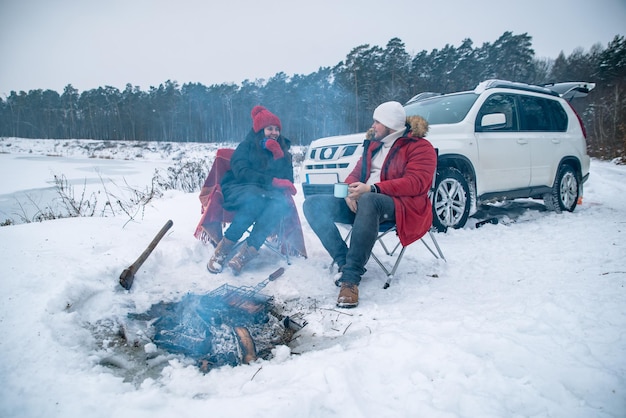 Man with woman sitting on chairs near camp fire in winter time\
car travel