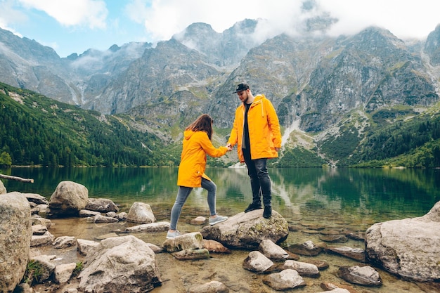 Man with woman in yellow raincoat at sunny autumn day looking at lake in tatra mountains