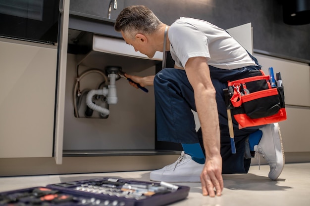 Man with wrench touching pipe under sink