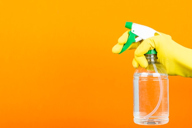 Man with yellow protective glove holding spray bottle for sanitizing orange background. Wiping down surface concept.