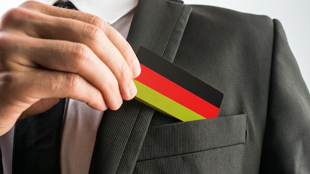 Man withdrawing a wooden card painted as the German flag from his suit pocket, close up of his hand.