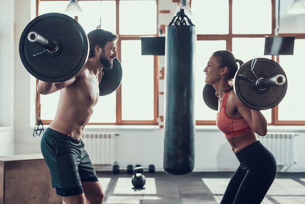 Photo man and woman are lifting barbells in the gym.