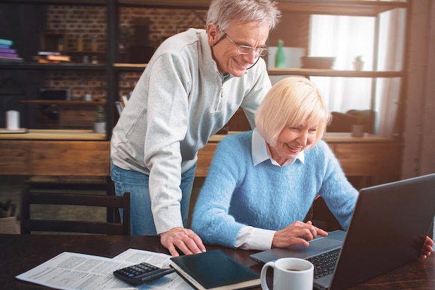 Man and woman are looking to the laptop's screen and laughing.