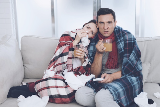 man and woman are sitting on couch and drinking tea.