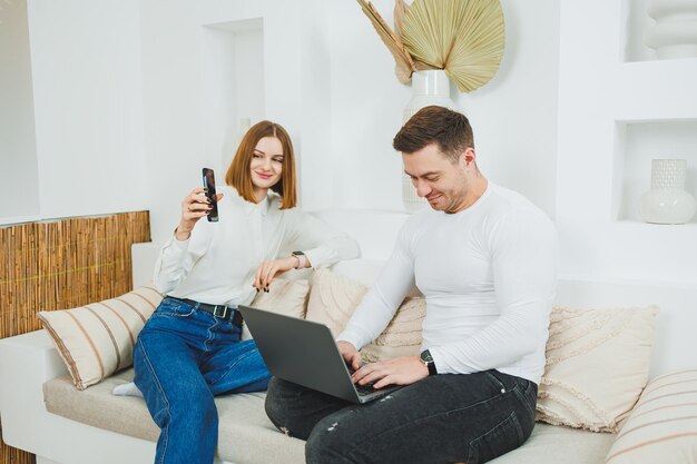 a man and a woman are sitting on the couch at home and watching a video on a laptop