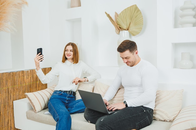 a man and a woman are sitting on the couch at home and watching a video on a laptop