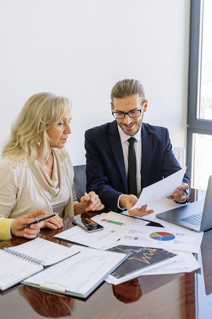 a man and woman are sitting at a desk with a laptop and a graph on it