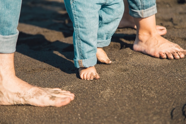 Man, woman and baby feet making steps on sand of beach