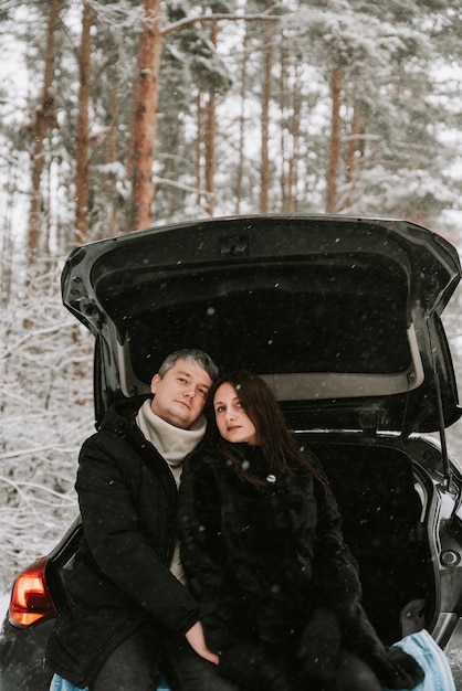 A man and a woman on the background of a snow-covered forest in a snowfall in the trunk of a car