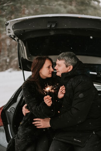 A man and a woman on the background of a snow-covered forest in a snowfall in the trunk of a car