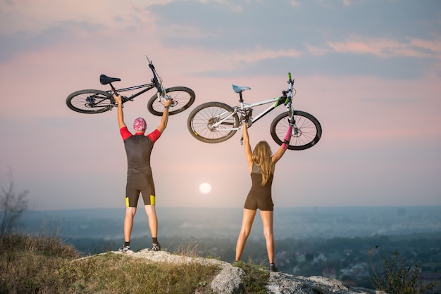 Man and woman bikers holding bikes high up