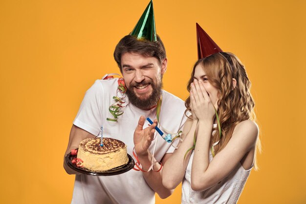 Man and woman birthday festive cake yellow background and caps on the headv person