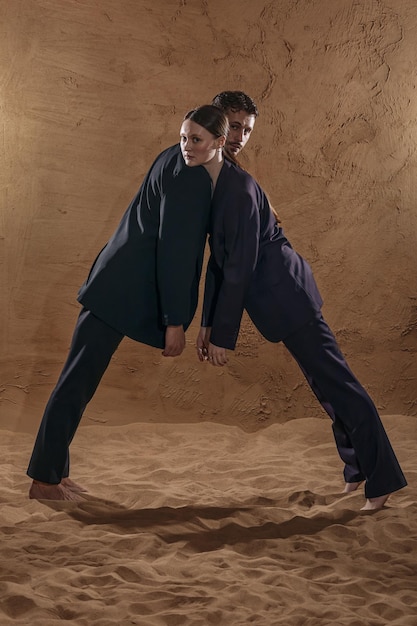 Man and woman both dressed in suits leaning towards each other on the sand cyclorama.