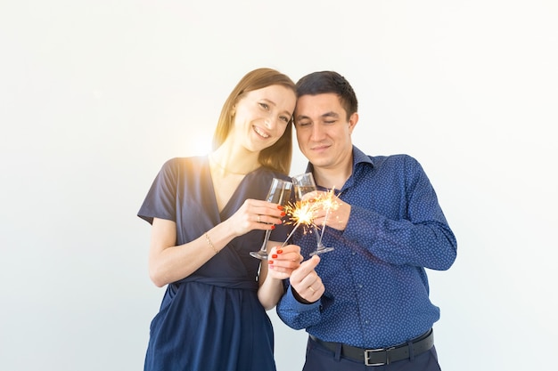 Man and woman celebrating Christmas or New Year eve party with Bengal lights and glasses of champagne on white background.