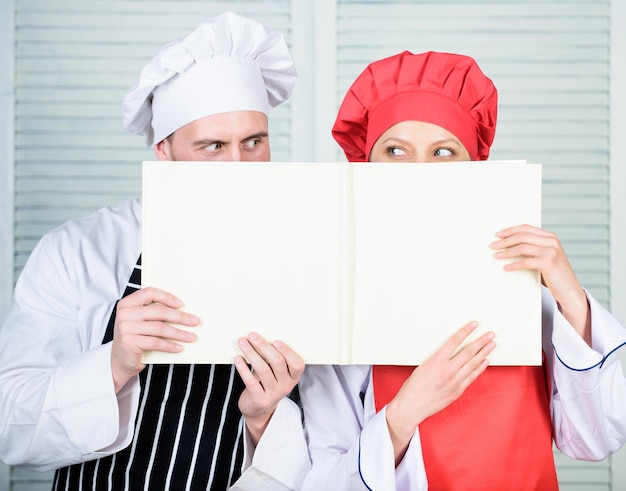 Foto l'uomo e la donna chef nascondono i volti dietro il libro aperto ragazzo e ragazza leggono le ricette del libro concetto culinario la famiglia impara la ricetta migliora l'abilità culinaria prenota le ricette di famiglia guida alla cucina secondo la ricetta