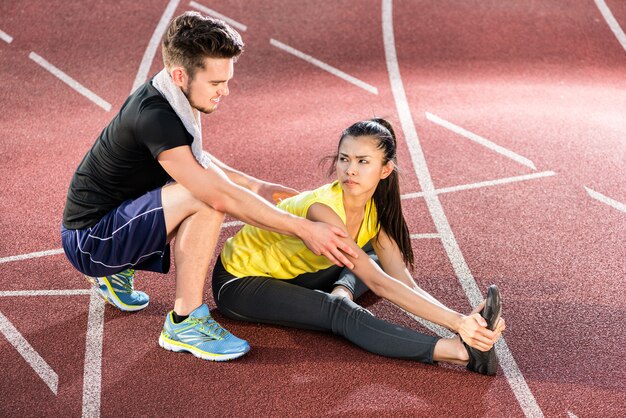 Man and woman on cinder track of sports arena stretching exercises