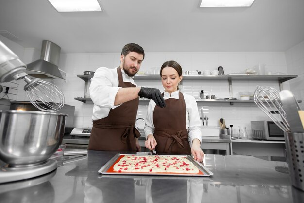 男性と女性がプロのキッチンで料理し、スポンジケーキにベリーを追加します