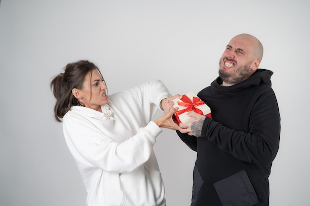 Man and woman couple on gray with a festive gift, take a gift from each other, pull, have fun, laugh