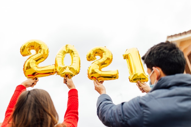 金箔風船数字2021を保持している男性と女性のカップル。新年のお祝いのコンセプト。
