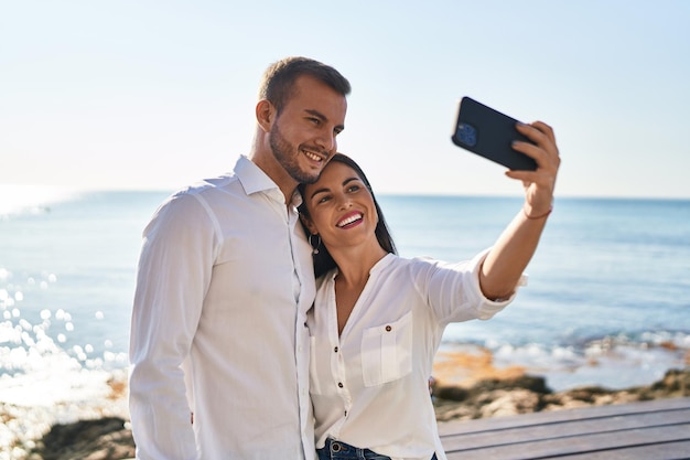 Man and woman couple hugging each other make selfie by the smartphone standing at seaside