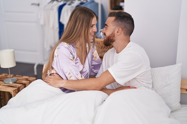 Man and woman couple sitting on bed hugging each other at bedroom