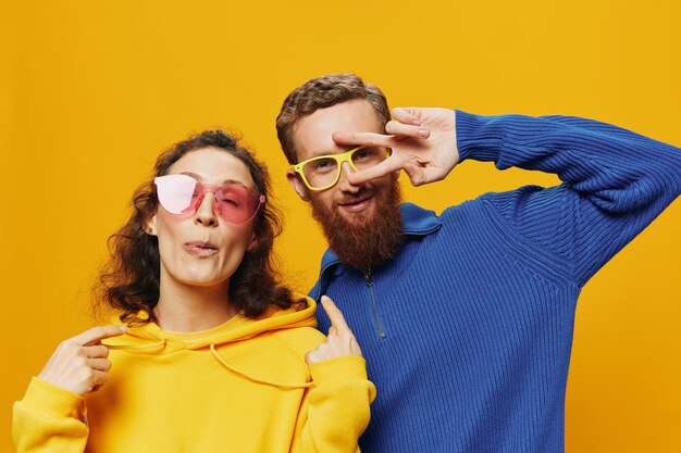 Man and woman couple smiling cheerfully and crooked with glasses on yellow background symbols signs and hand gestures family shoot newlyweds