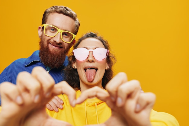 Man and woman couple smiling cheerfully and crooked with glasses on yellow background symbols signs and hand gestures family shoot newlyweds