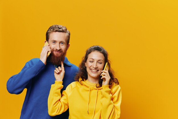 Man and woman couple smiling merrily with phone in hand social media viewing photos and videos on yellow background symbols signs and hand gestures family freelancers