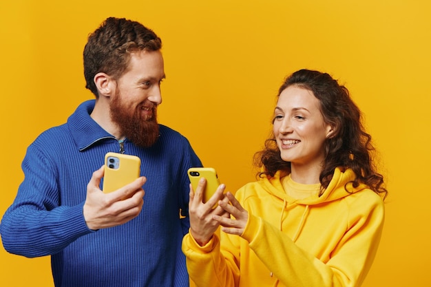 Man and woman couple smiling merrily with phone in hand social media viewing photos and videos on yellow background symbols signs and hand gestures family freelancers