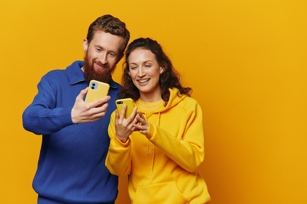 Man and woman couple smiling merrily with phone in hand social media viewing photos and videos on yellow background symbols signs and hand gestures family freelancers