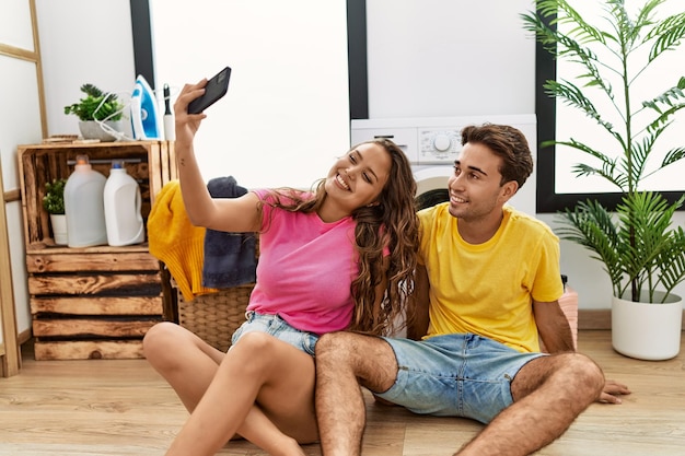 Man and woman couple waiting for washing machine making selfie by the smartphone at laundry room