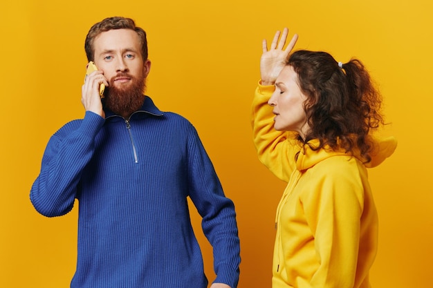 Мужчина и женщина пара с телефоном в руке, звонок, разговор по телефону на желтом фоне, символы, знаки и жесты рук, семейная ссора, ревность и скандал
