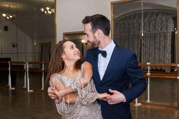 Man and woman dance, looking at each other, in large empty ballroom