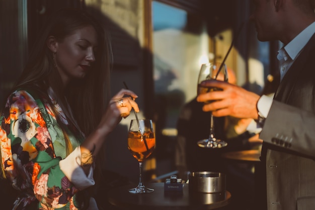 Man and woman drink cocktails in a street cafe on the summer terrace. Elegant couple drinks aperol spritz.