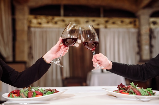 Man and woman drinking red wine. In the picture, close-up hands with glasses.