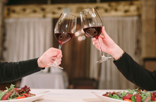 Man and woman drinking red wine. In the picture, close-up hands with glasses.