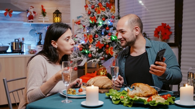 Man and woman eating festive dinner looking at smartphone