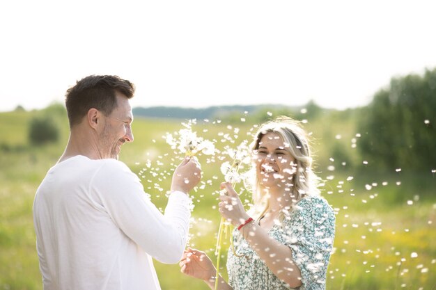 Man and woman in the field blowing dandelions, young family concept