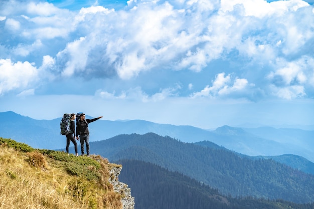 The man and a woman gesturing on the cliff with a beautiful view