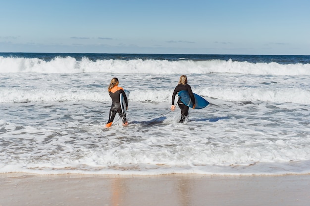 man and woman go to the ocean with surf boards. man and girl go surfing