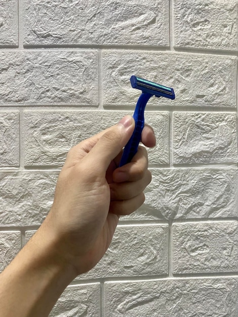 Foto una mano di uomo-donna che tiene un rasoiatore metallico blu per il trattamento personale dei capelli della barba e dei baffi