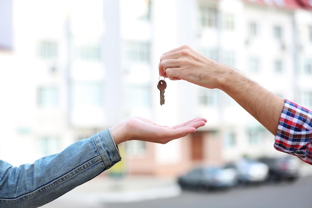 Man and woman hands hold keys near apartment house