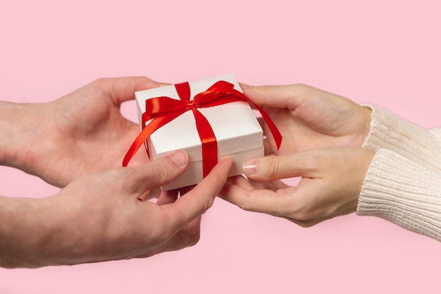 Photo man and woman hands holding gift box with red bow on pink