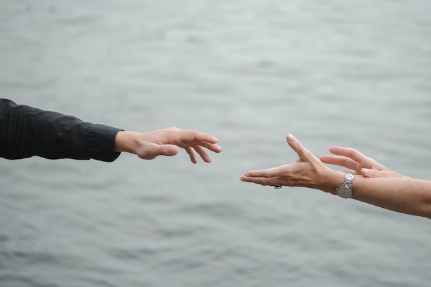 Man and woman hands reaching out holding near water