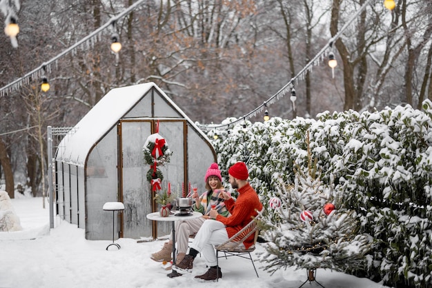 Man and woman have romantic dinner while sitting together by the table at beautifully decorated snowy backyard Young family celebrating winter holidays