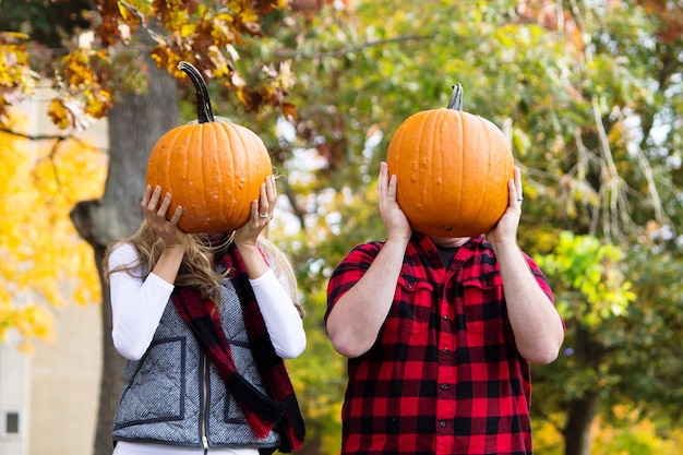 Photo man and woman hiding face with pumpkins against trees in yard